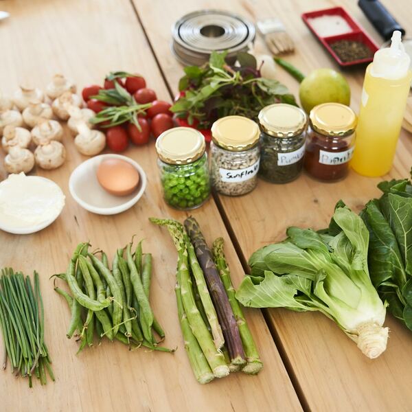 Groente uitgestald op een licht houten tafel: sperziebonen, tomaten, paksoi, asperges, een ei en een paar potjes kruiden.